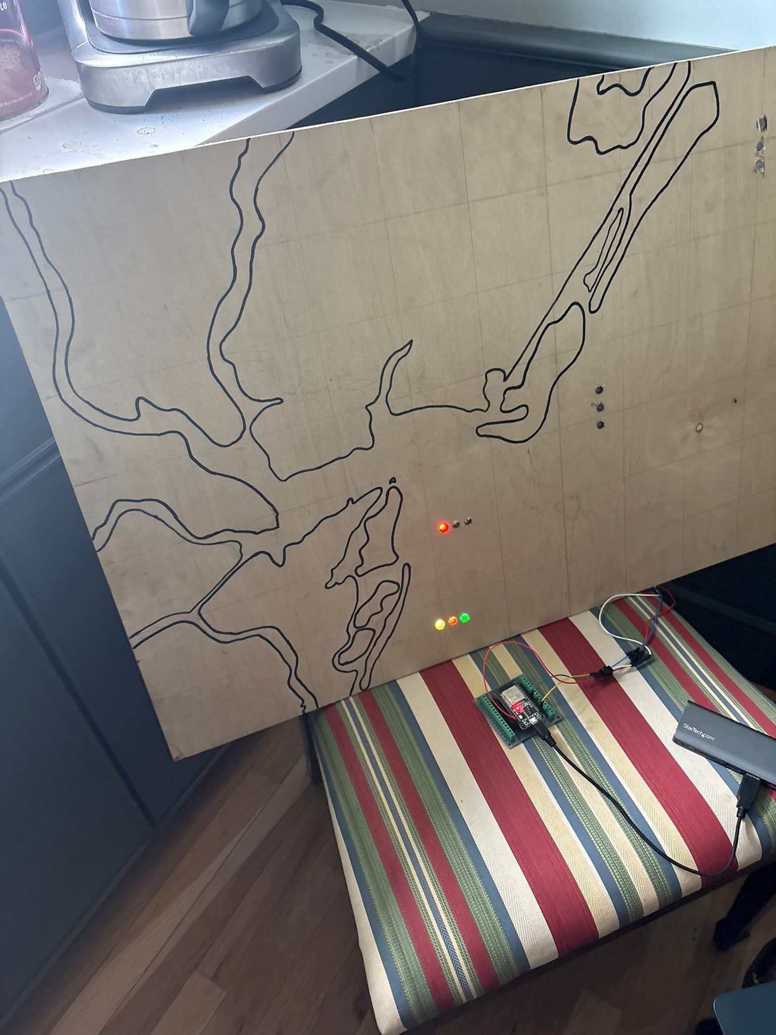 An early plywood prototype with a traced coastline, lit LEDs, and a microcontroller wired up on a chair.